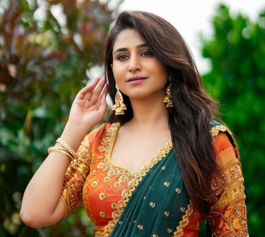 Varshini Sounderajan in a green and orange half saree with gold bangles, outdoors